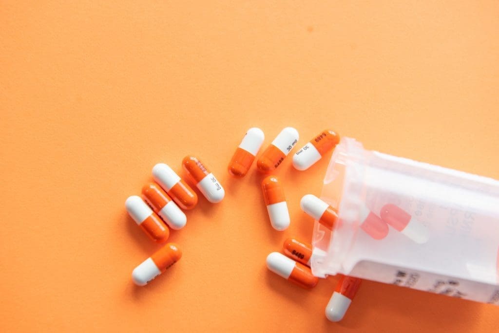 Orange and white pills falling out of a container on an orange background.