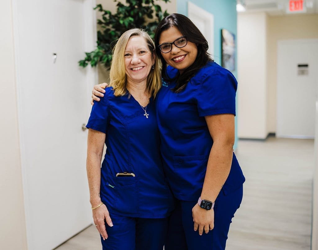 Two women in blue scrubs posing for a photo.