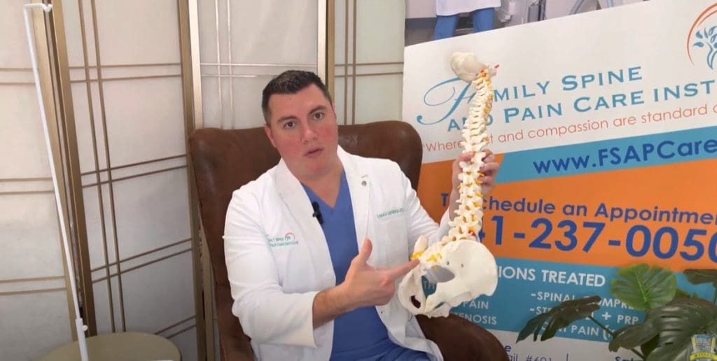 A man in a white coat is holding a model of a spine.